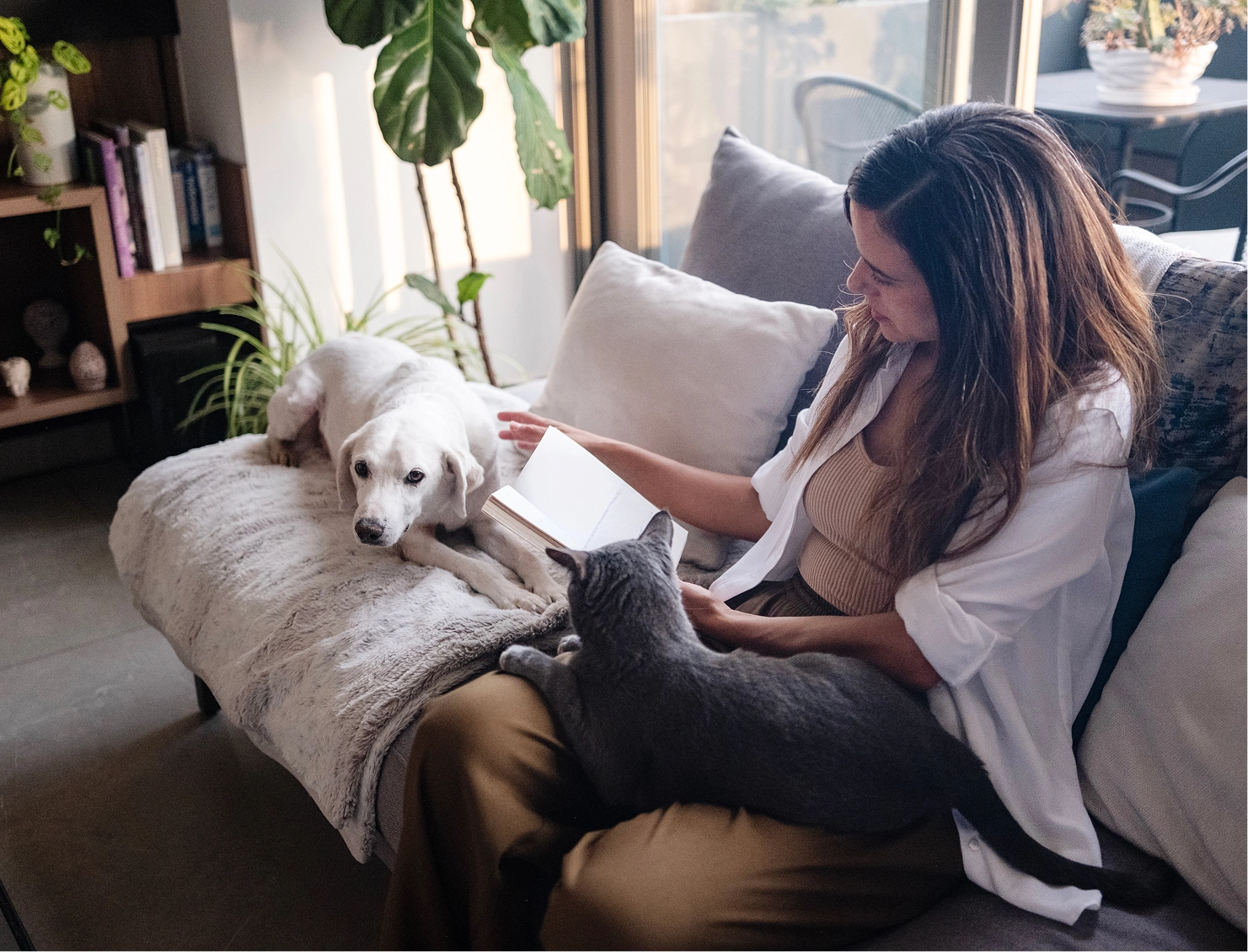 Woman reading with dog and cat nearby.