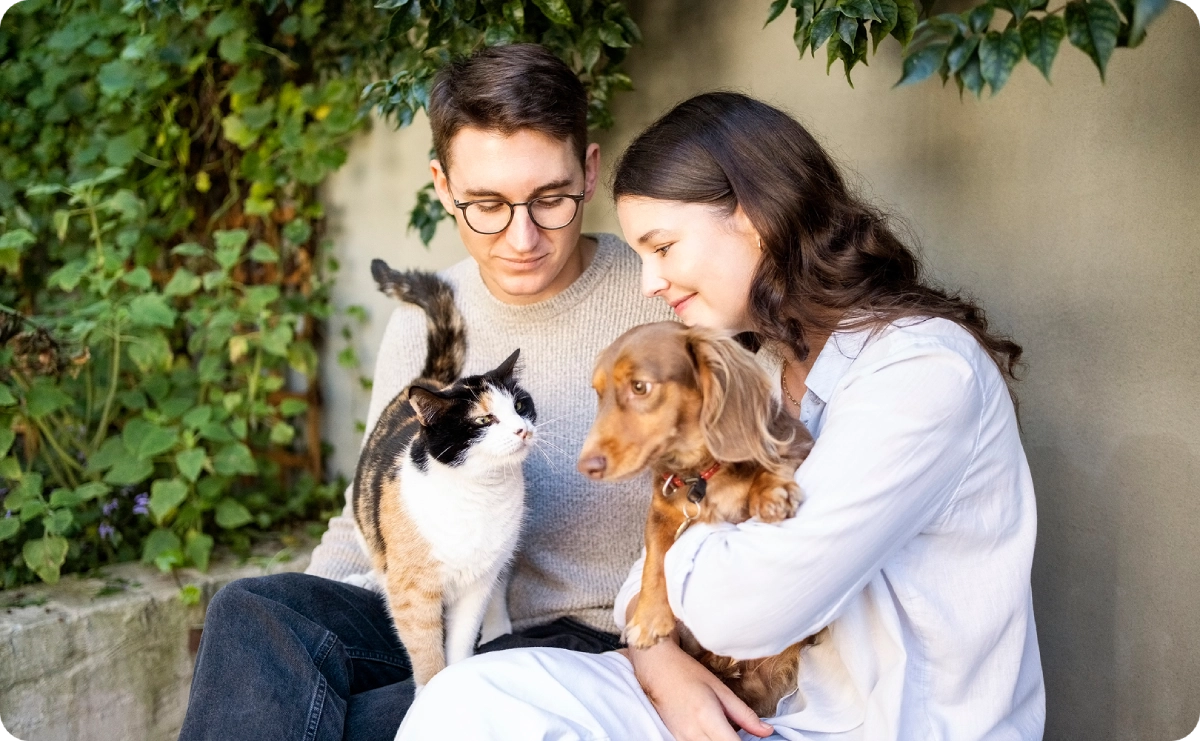 Couple sitting with cat and dog outside.
